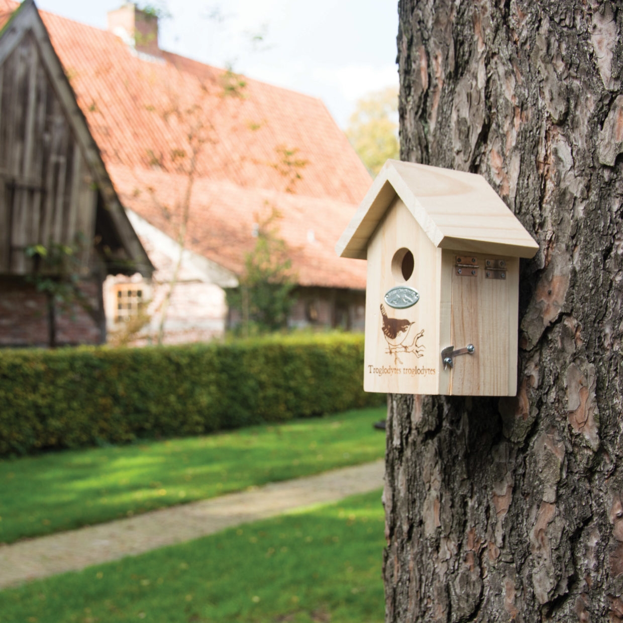 Een houten vogelhuisje hangt aan een boom in een groene tuin.